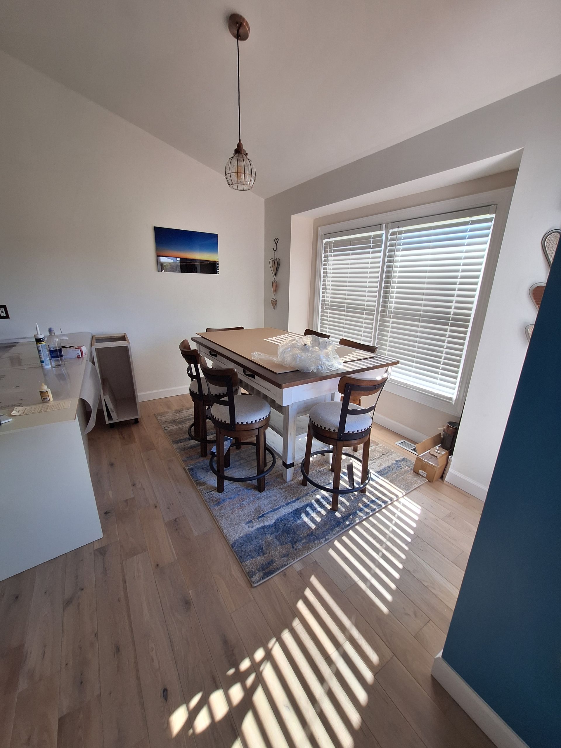 Bright dining room with wooden table, chairs, large window blinds, and sunlight on the floor