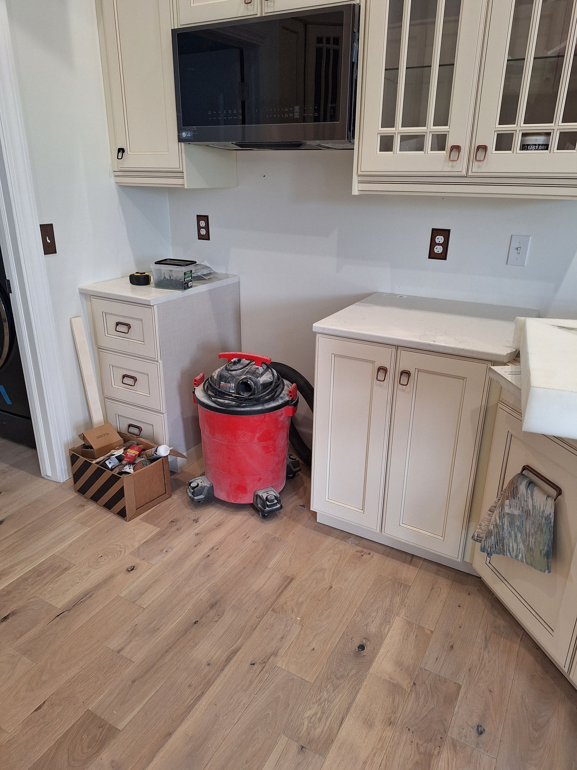 Renovated kitchen with white cabinets, gray countertop, and a red trash can on wood flooring