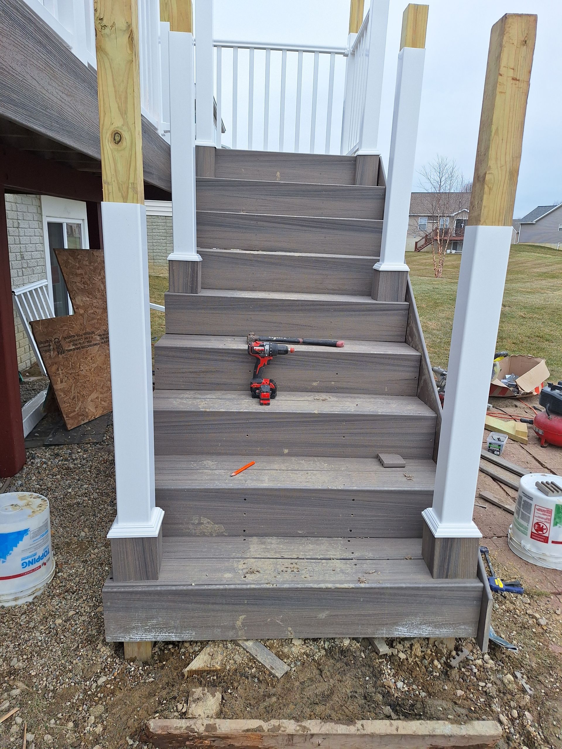 Unfinished front steps with gray treads and white railings, plus a red toy on the stairs.