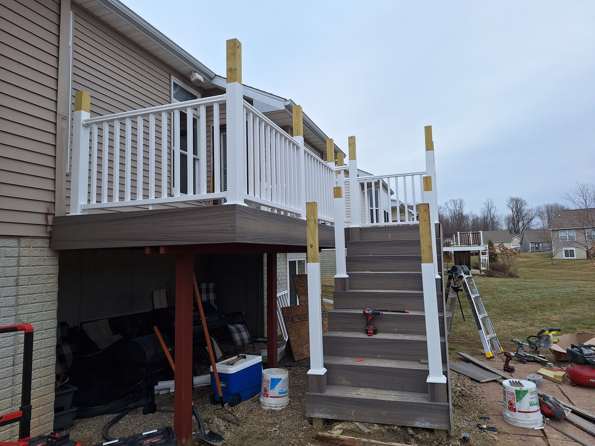 Backyard deck under construction with stairs, white railing, and support posts beside a house.