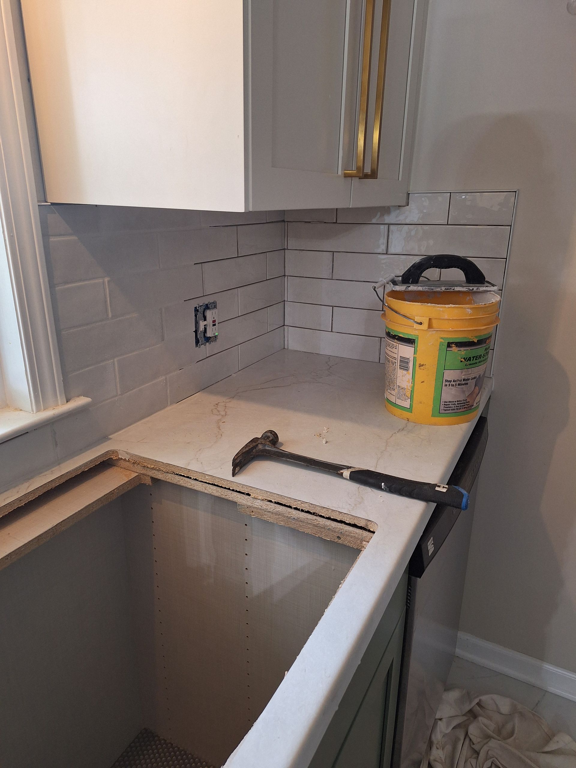 Partially renovated kitchen with sink, gray backsplash tiles, and a yellow paint bucket on the counter