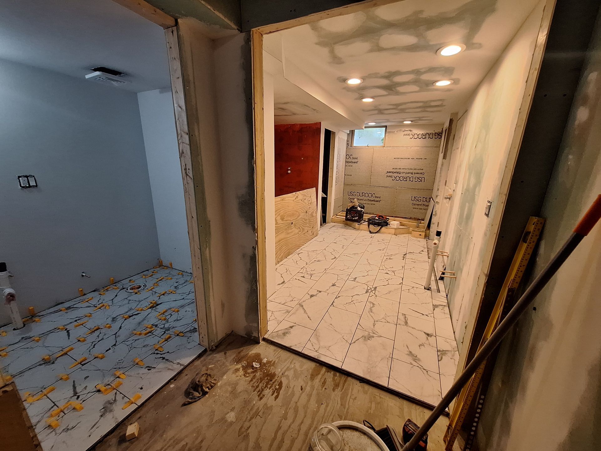 Renovation site with two rooms, white tiled floor, exposed walls, and scattered tools and debris