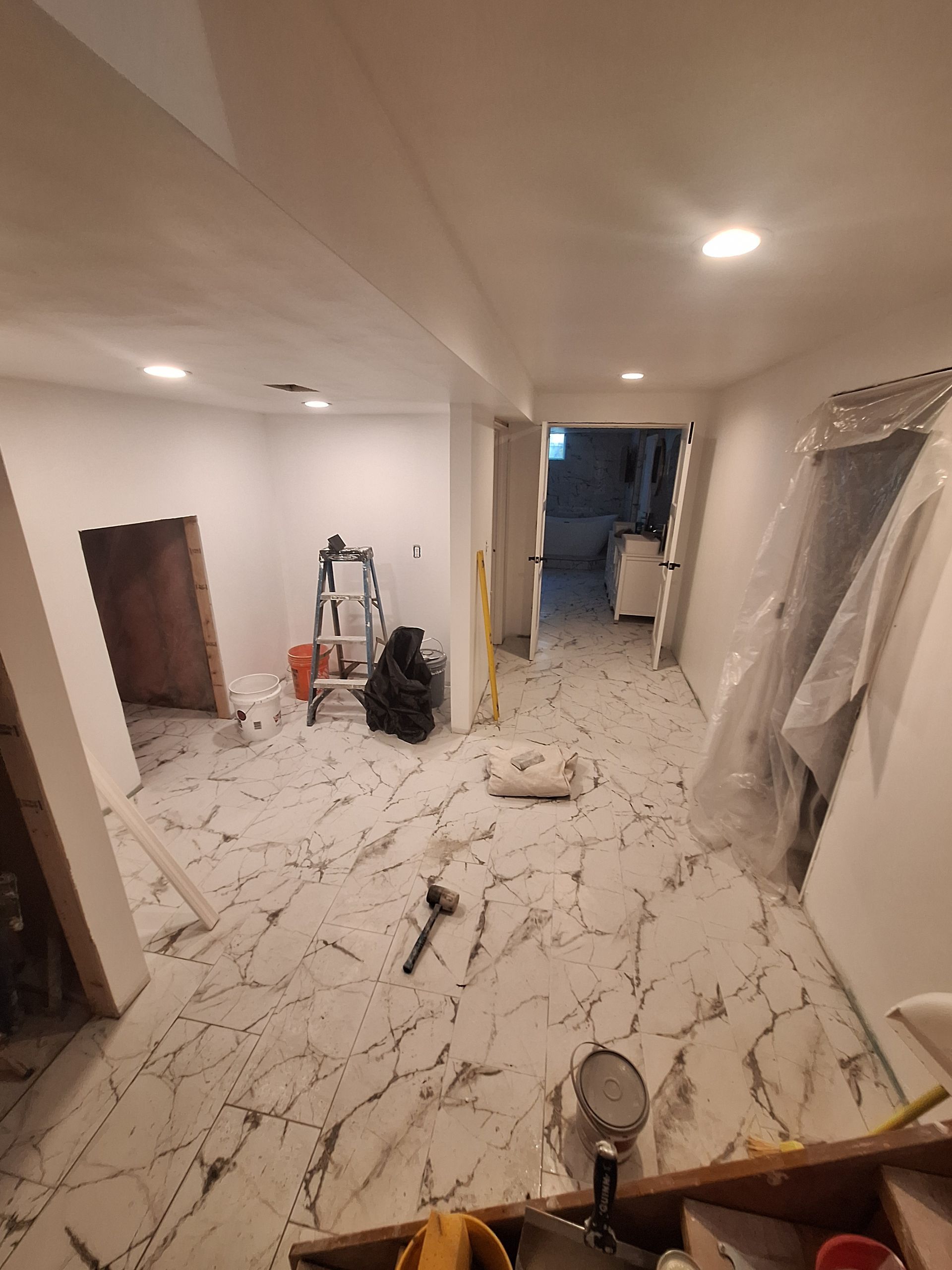 Renovation in progress in a white hallway, with tools, covered furniture, and debris on the floor.