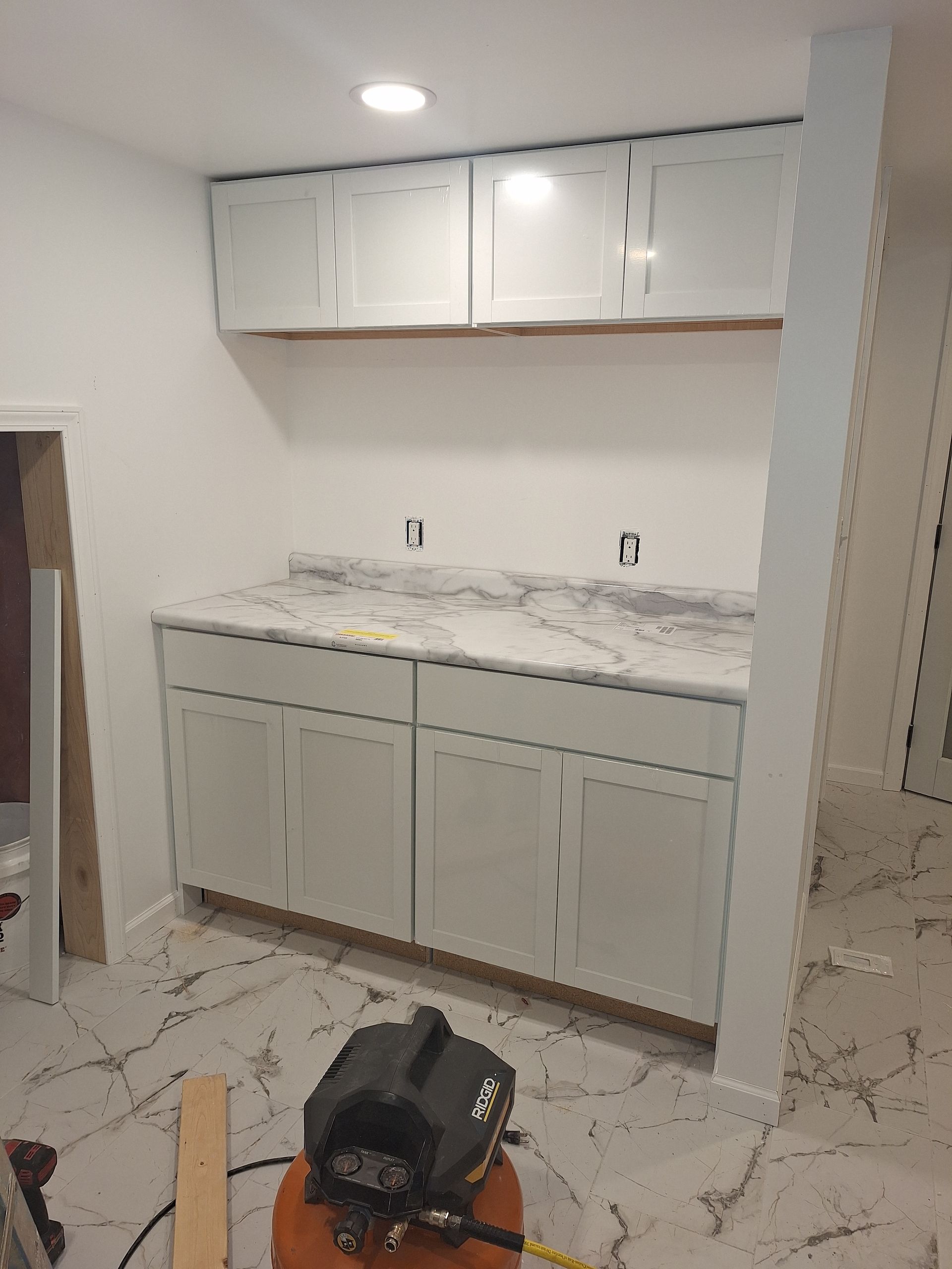 Partially finished kitchen with white cabinets, marble-look countertops, and tools on the floor