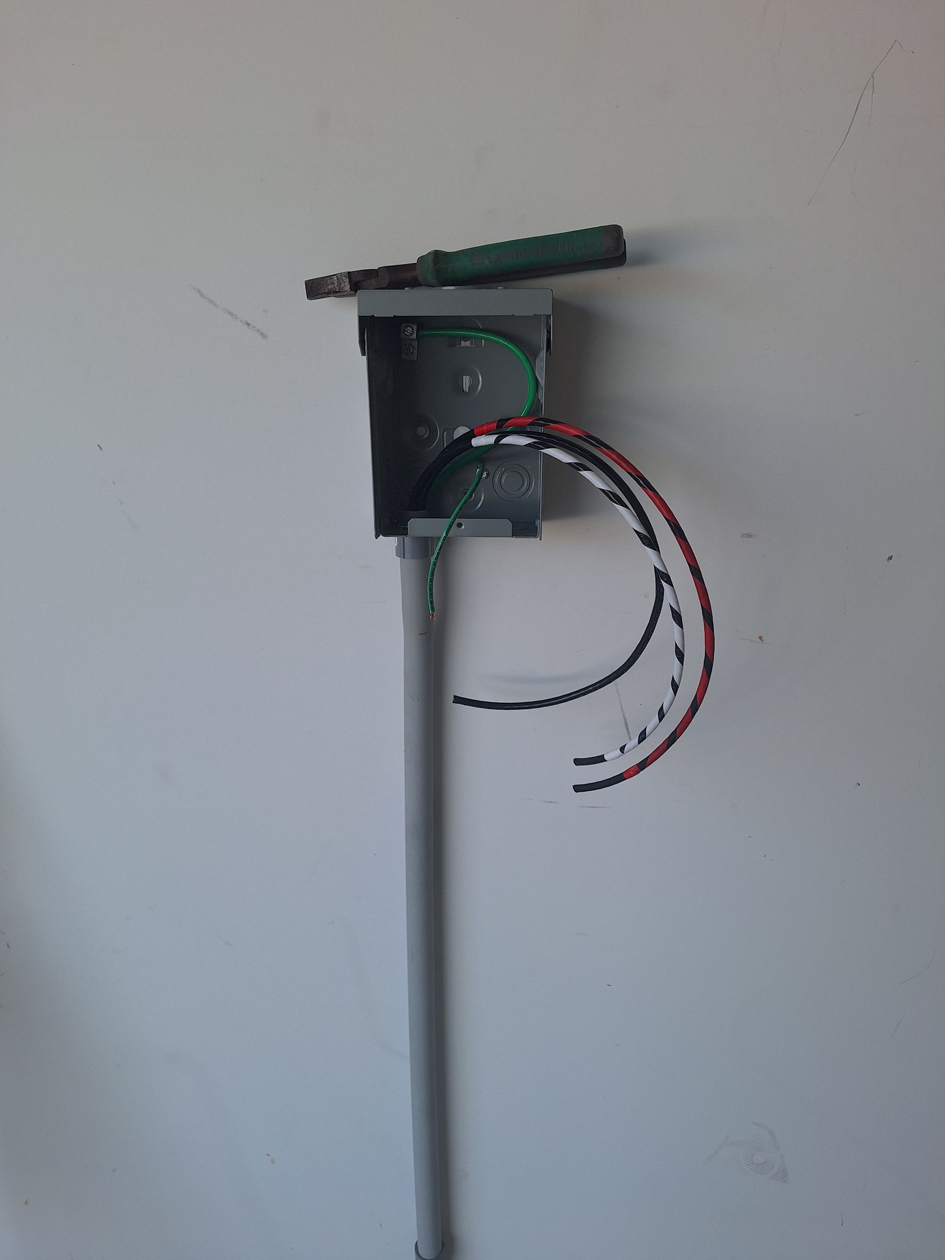 Wall-mounted electrical box with exposed red, black, and white wires against a white wall