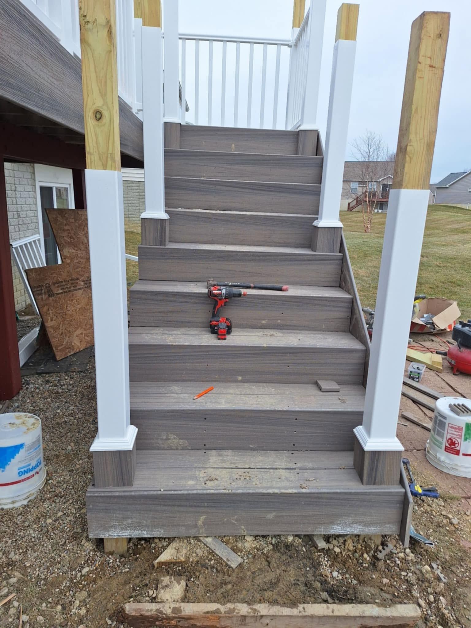 Wooden staircase under construction with a red drill on the steps and white railings on both sides