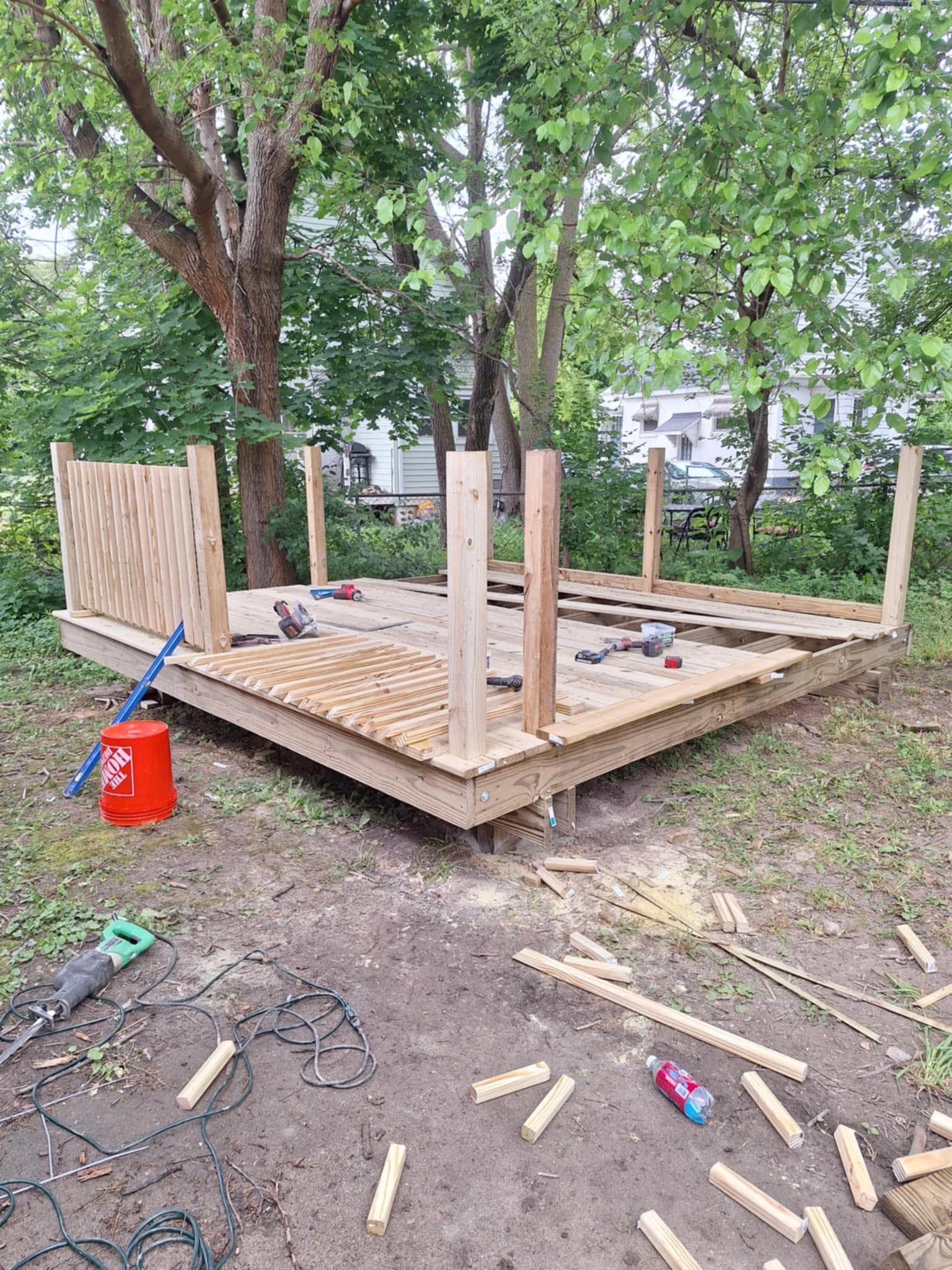 Partially built wooden deck in a yard, with tools and lumber under trees.