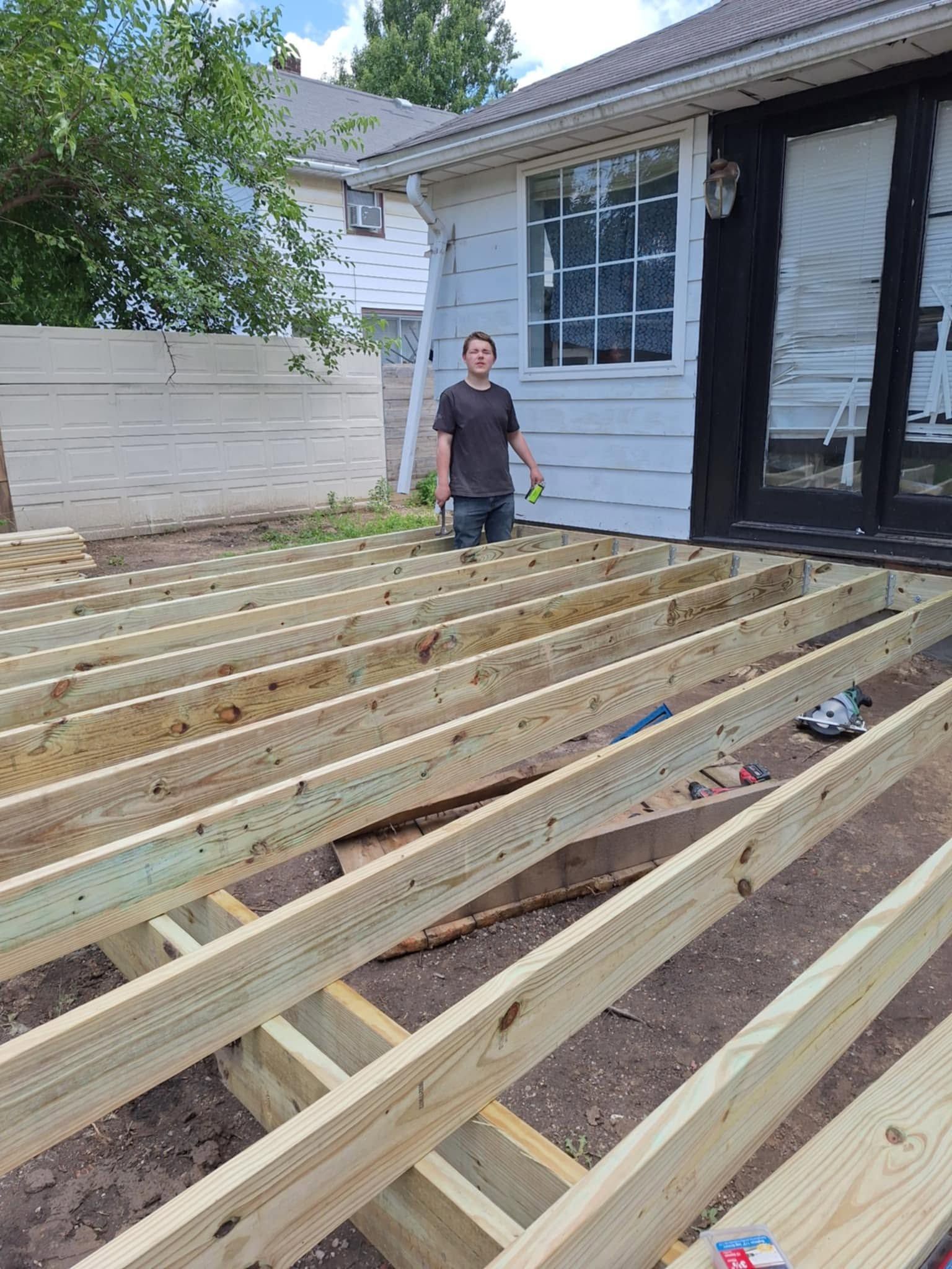 Person standing on newly installed wooden deck framing beside a house