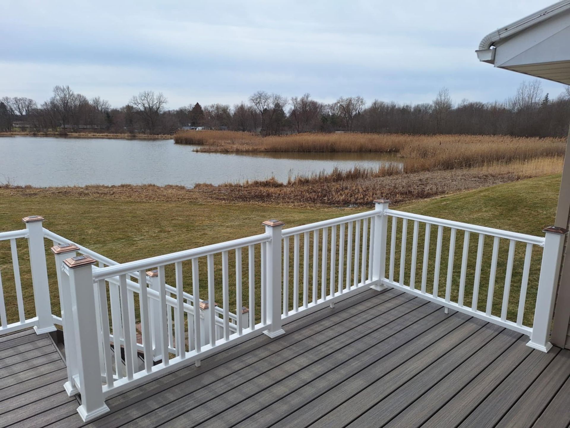 White deck overlooking a pond and marsh with gray sky and bare trees