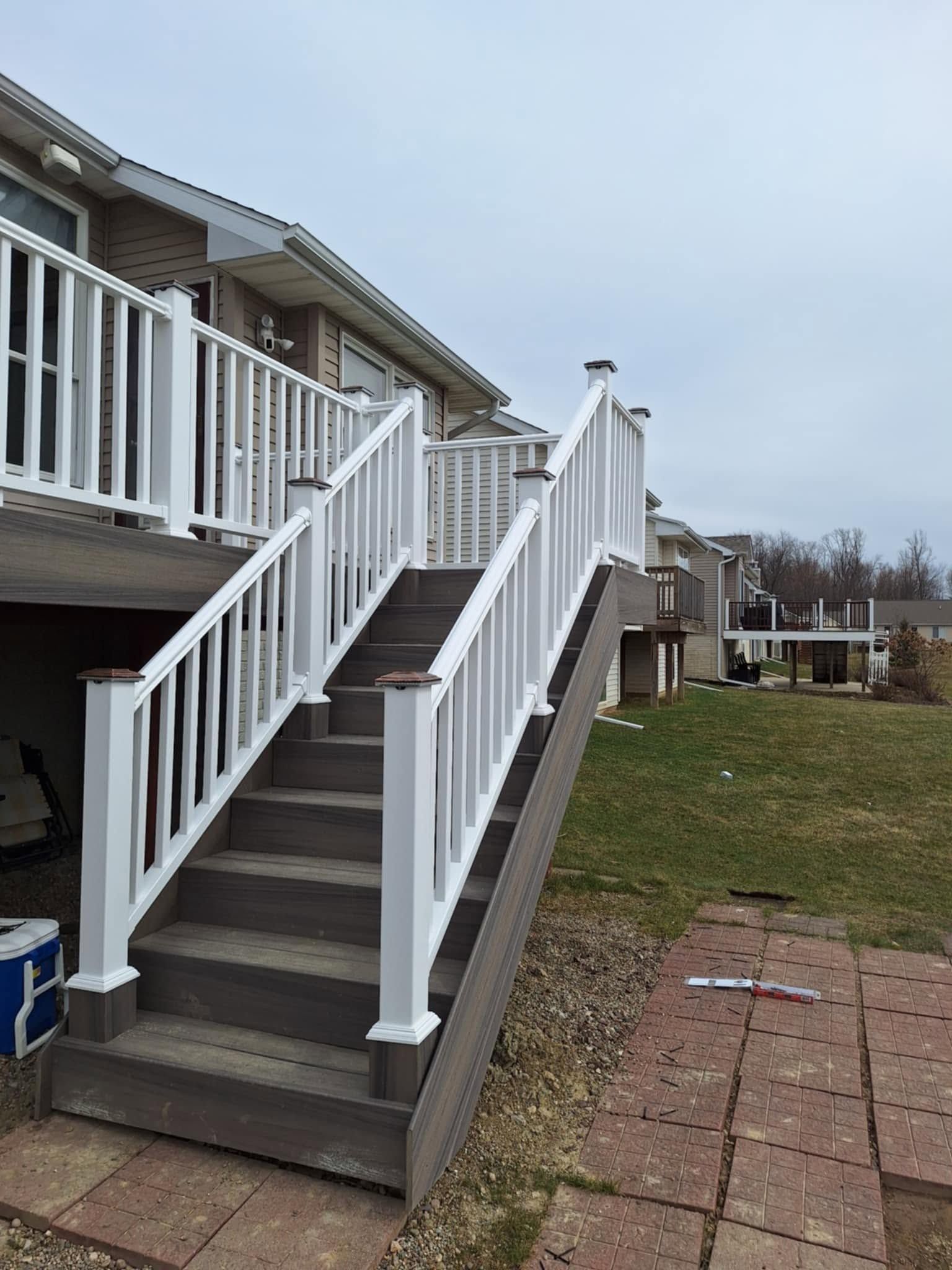 Front steps with white railings leading to a raised porch beside a brick-paved yard and grassy area.