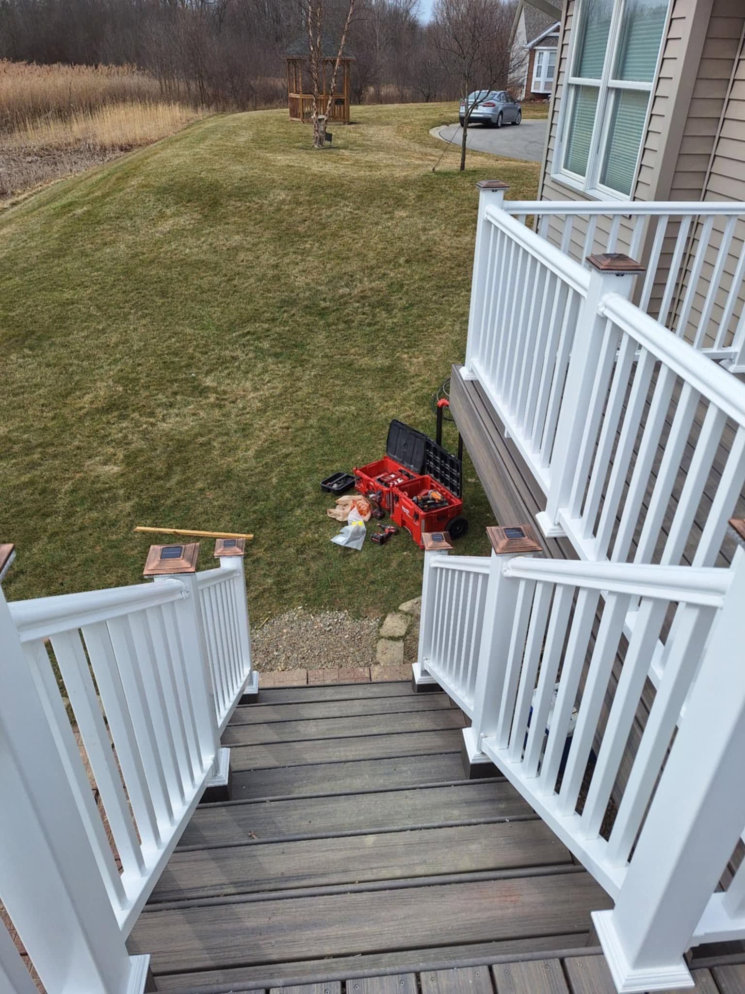 Wooden deck stairs leading to a grassy yard, with white railings and red flowers at the bottom.