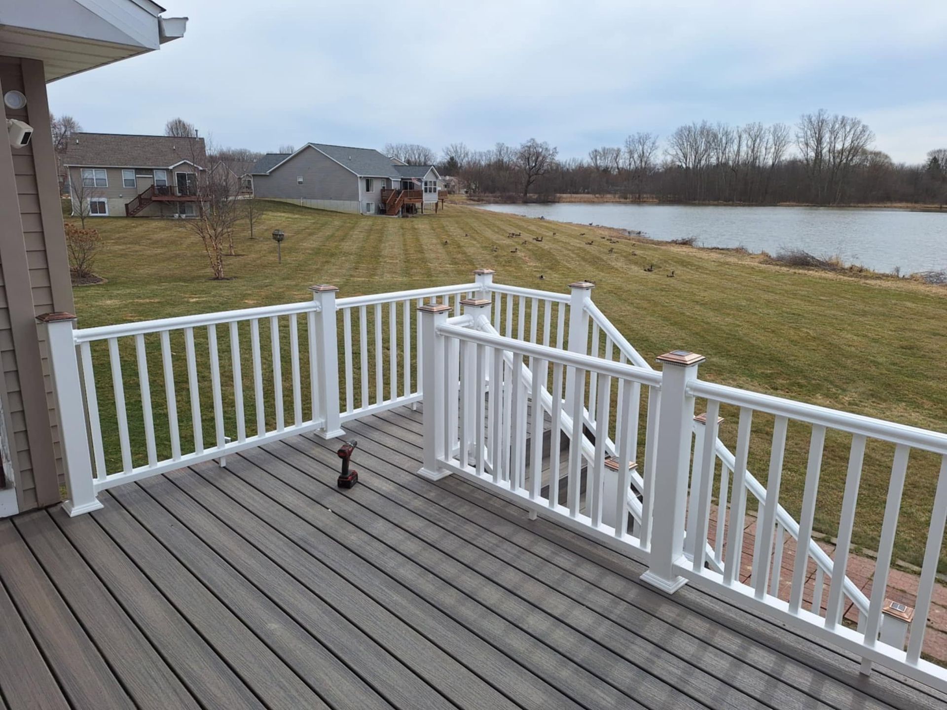 Deck with white railings overlooking a grassy yard and pond under an overcast sky.