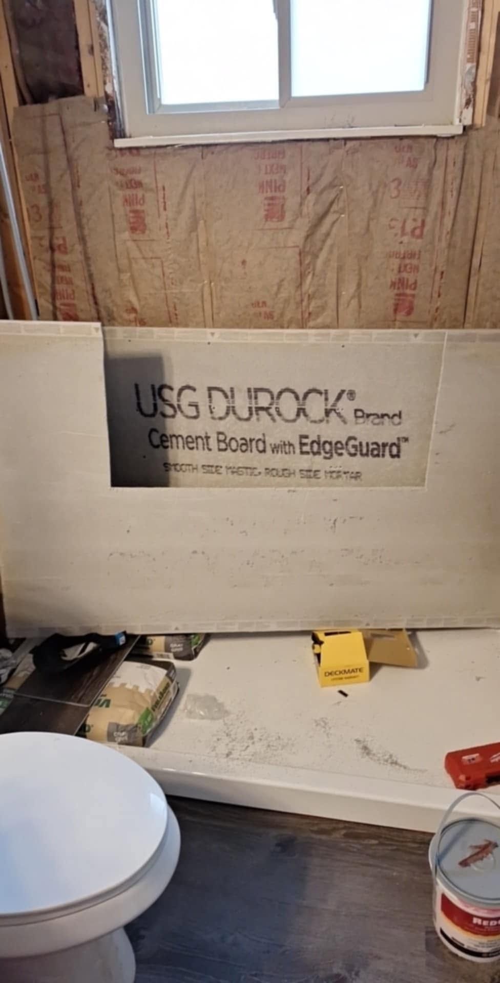 Bathroom wall under renovation with USG Durock cement board beneath a window and toilet in foreground