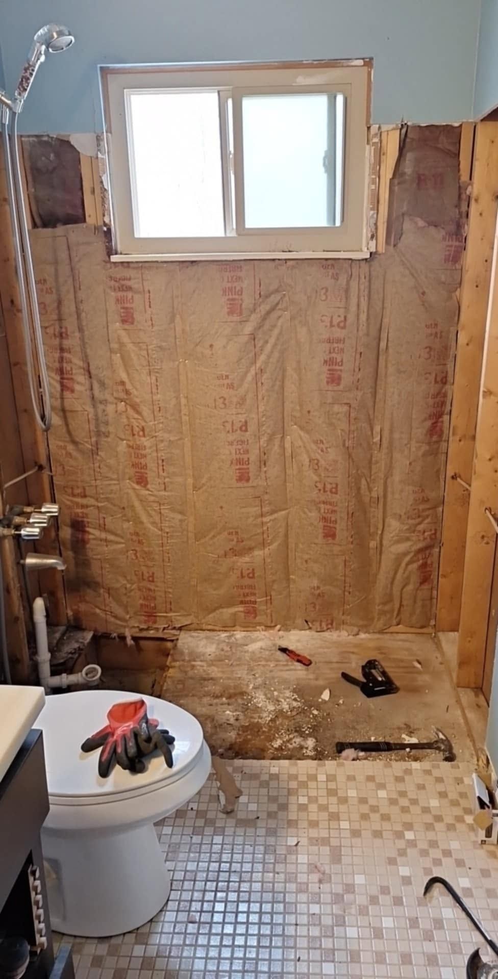 Partially gutted bathroom with exposed insulation, tiled floor, toilet, and window.