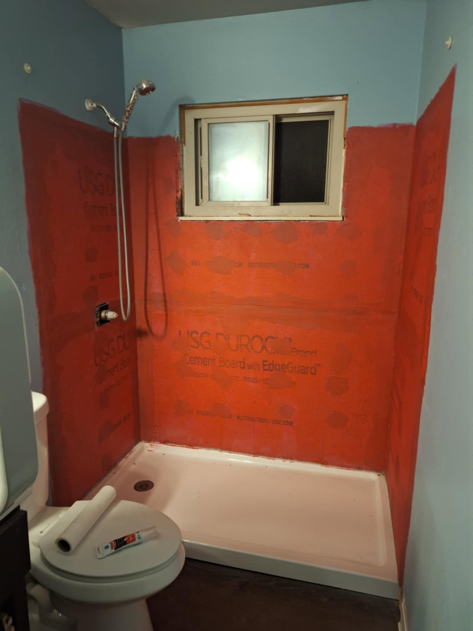 Small bathroom with orange walls, shower stall, toilet, and window.