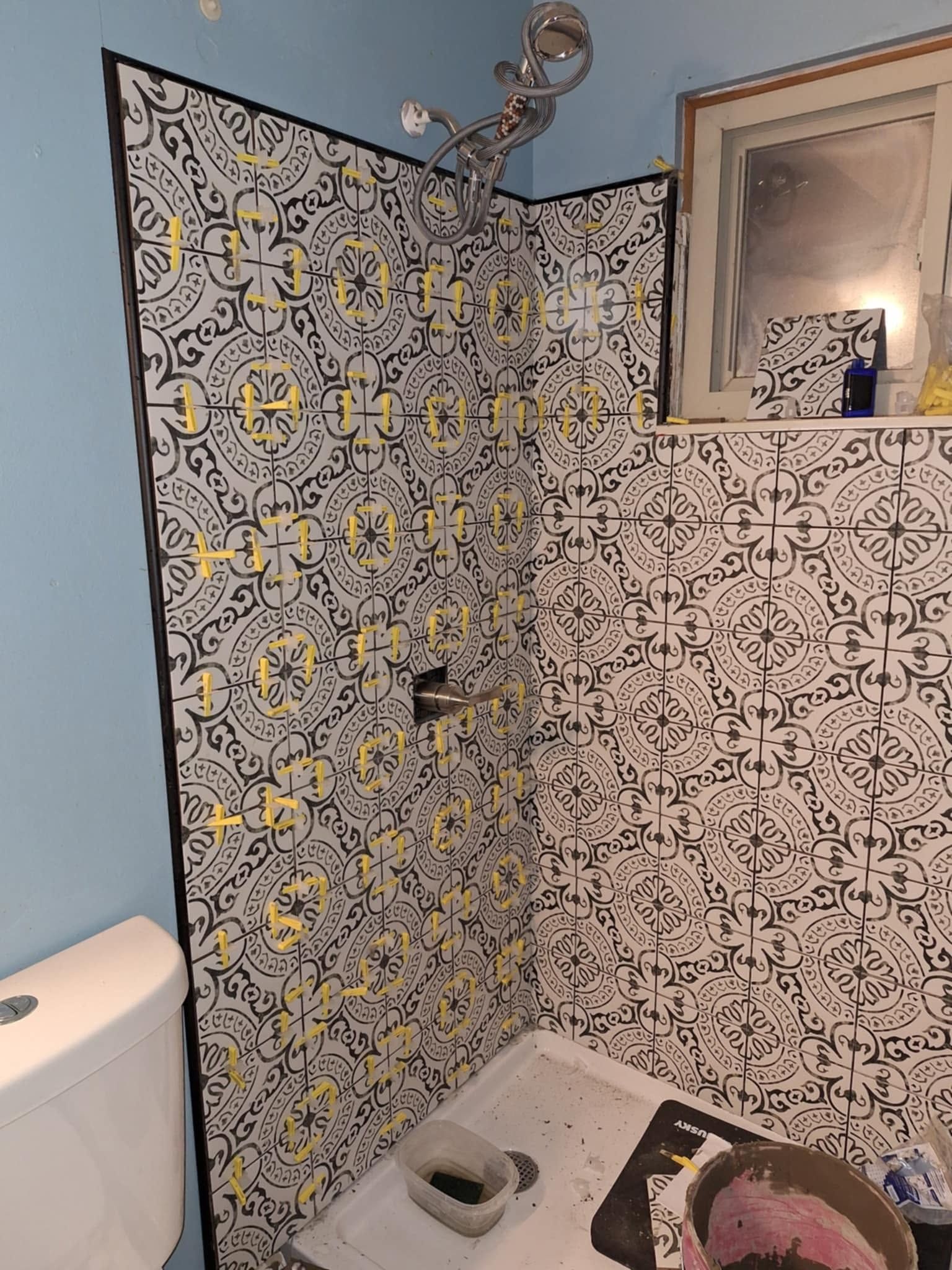Small bathroom shower area with patterned tile, toilet, and sink mirror.