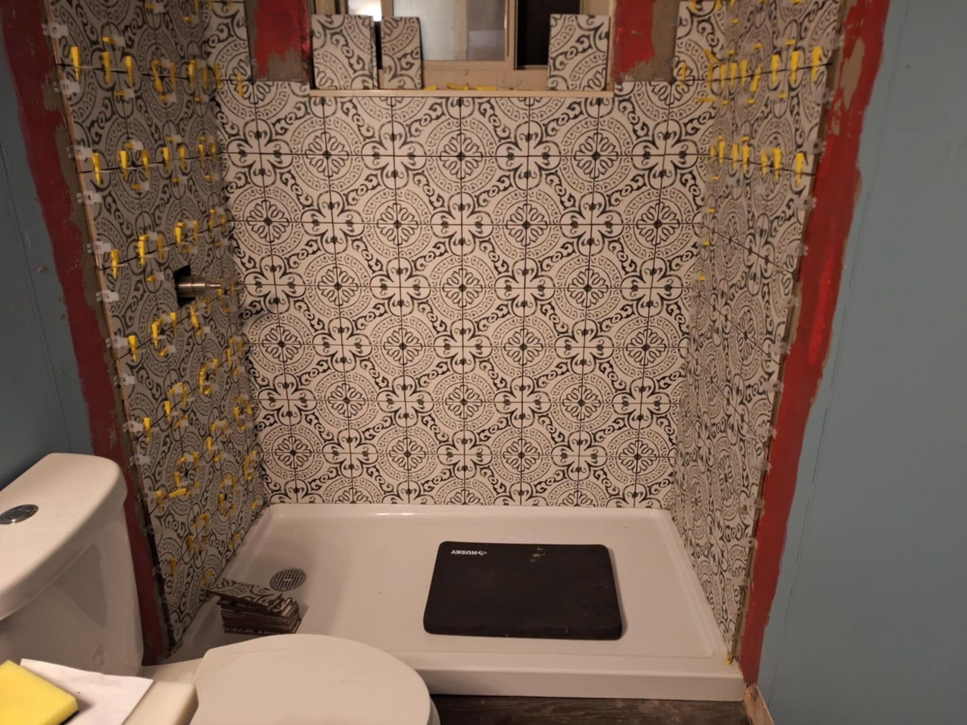 Small bathroom shower area with patterned tile walls and a white tub surround.