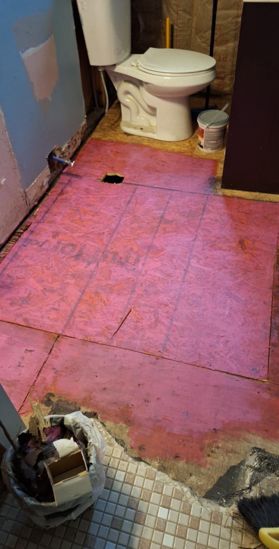 Small bathroom with a pink subfloor, exposed floor damage, and a toilet at the back.