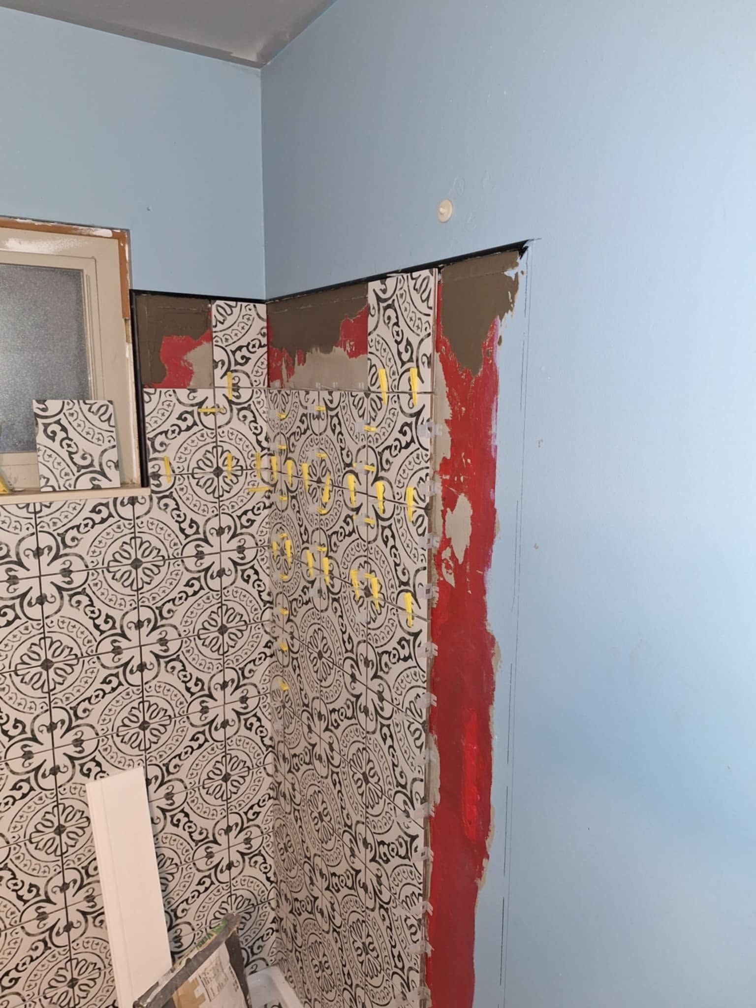 Partially renovated room with blue walls and exposed patterned wallpaper, red paint strip, and a small window opening
