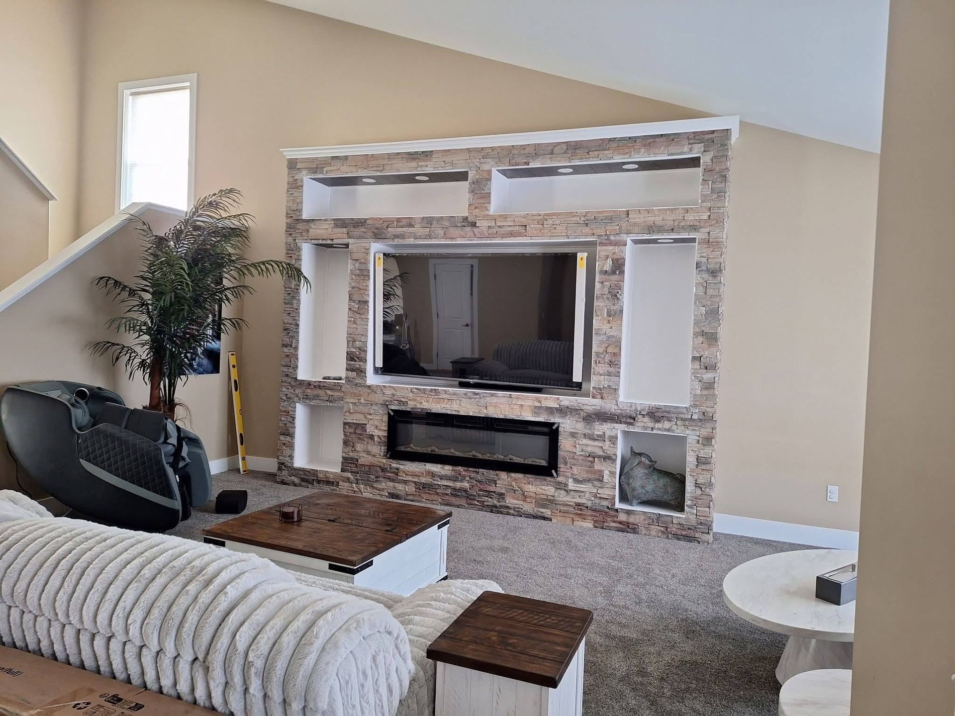 Living room with stone fireplace, wall-mounted TV, beige sofa, and large windows