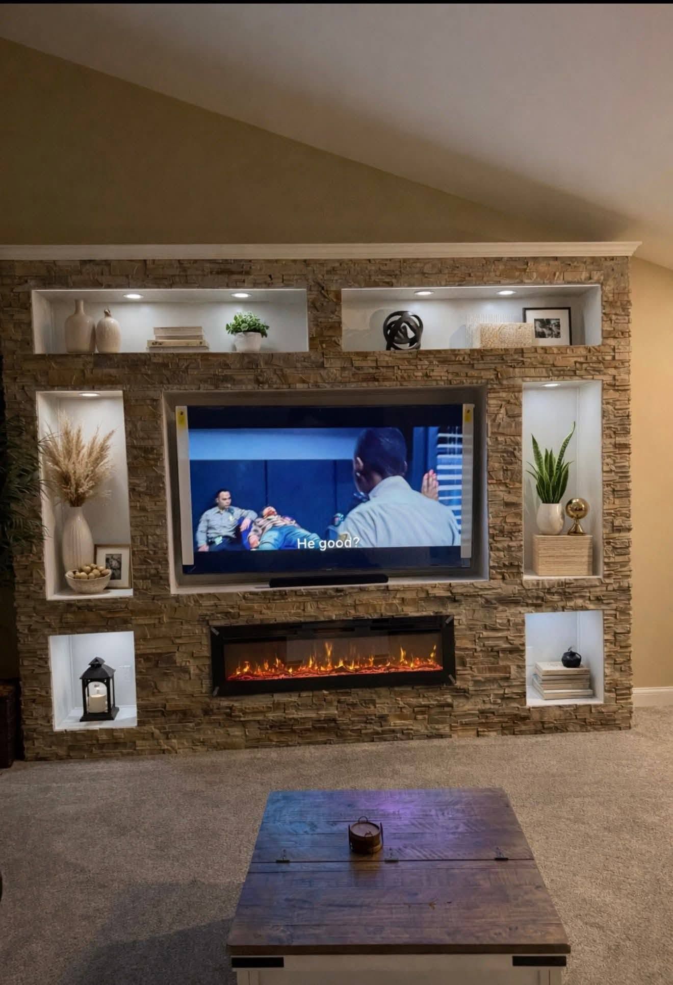 Living room with stone fireplace, mounted TV, and built-in shelves with decor