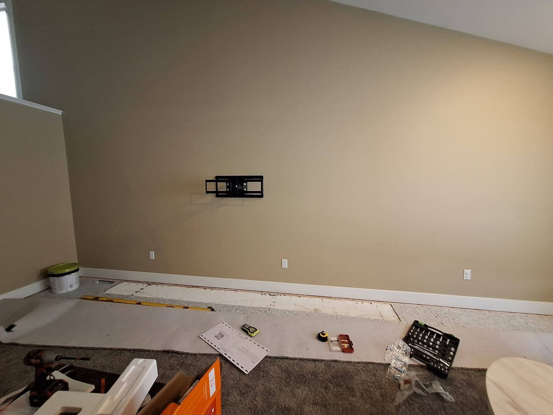 Empty room with beige wall, mounted TV bracket, and scattered renovation materials on the floor