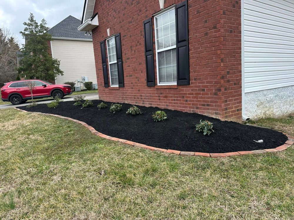 Red brick house with black shutters, a landscaped bed of black mulch, and a red car in the background.
