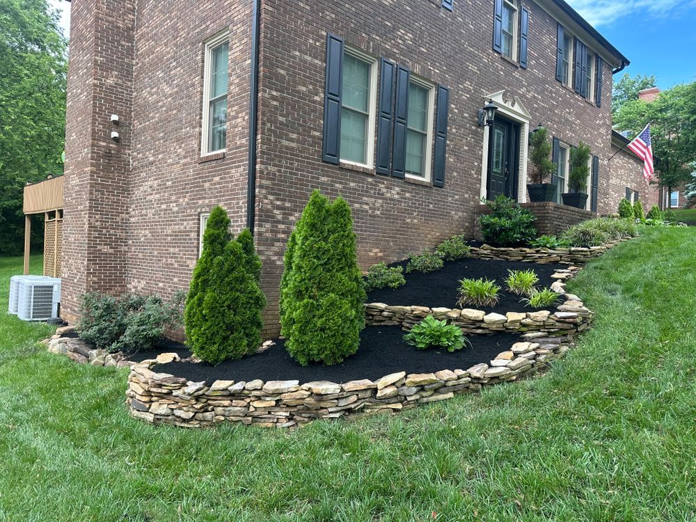 A two-story brick house with a stone-tiered garden bed and manicured lawn.