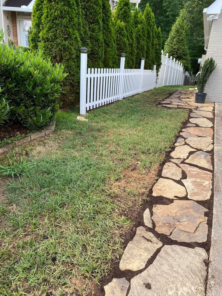 A flagstone path alongside a lawn and white picket fence; evergreen trees in the background.