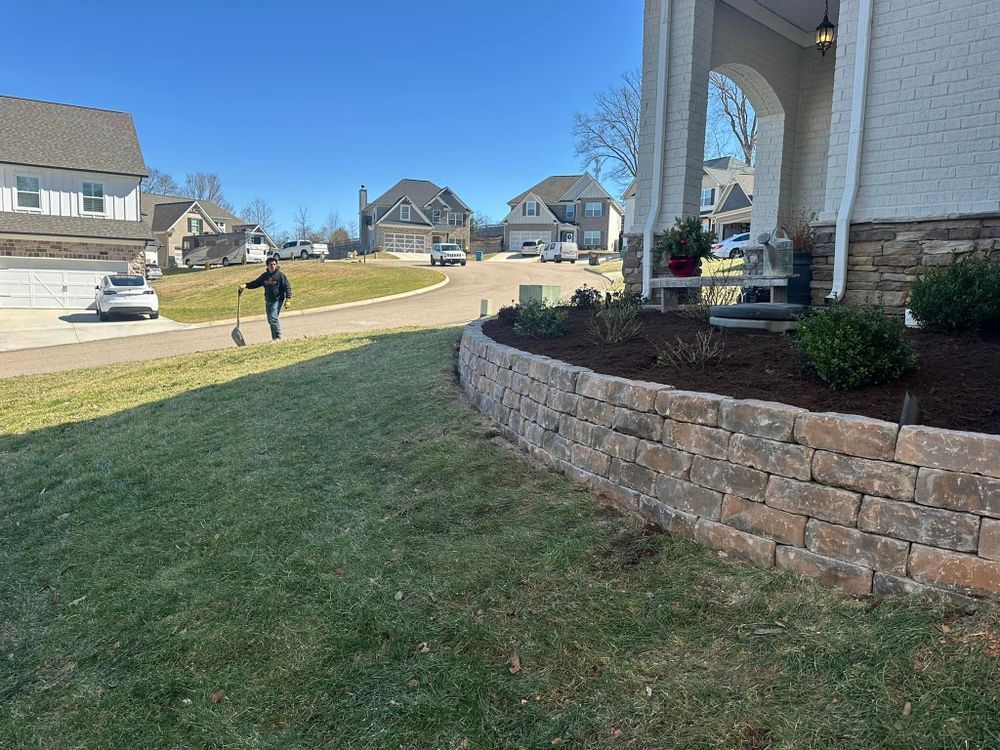 Man walking on a grassy hill in a residential neighborhood. Stone retaining wall and houses in the background.