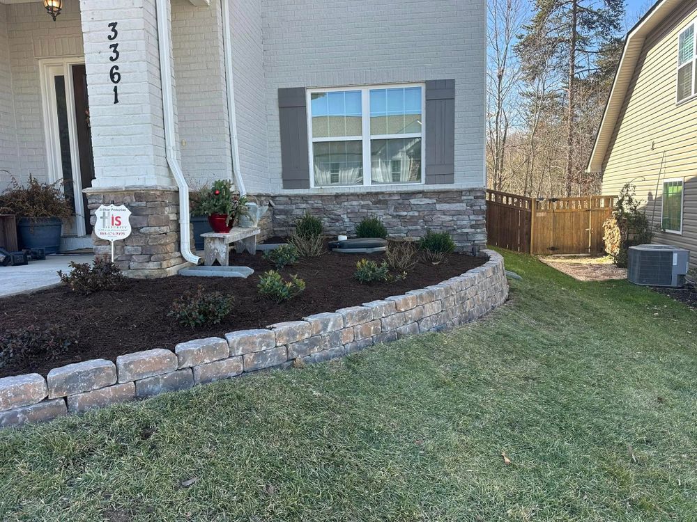 A house with a stone retaining wall, small plants, and a well-maintained lawn.