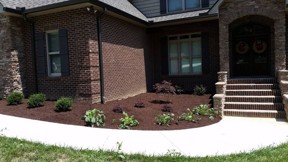 Brick home with landscaped bed, dark mulch, and green plants along a sidewalk.