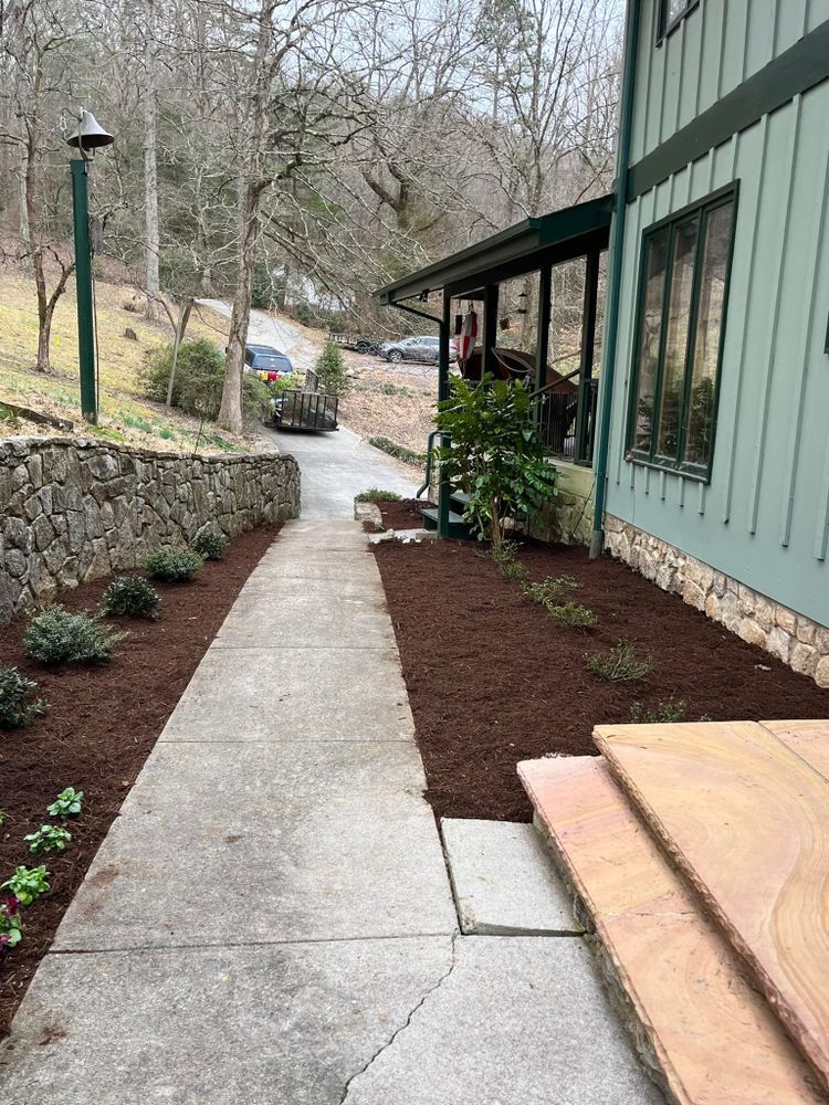 A concrete path flanked by landscaping and stone wall leads to a green building with a porch.
