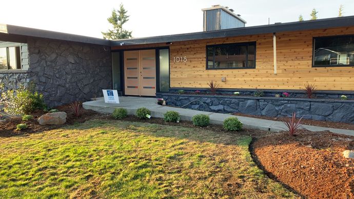 Modern single-story house with wood and stone facade, front door, windows, and a landscaped yard.