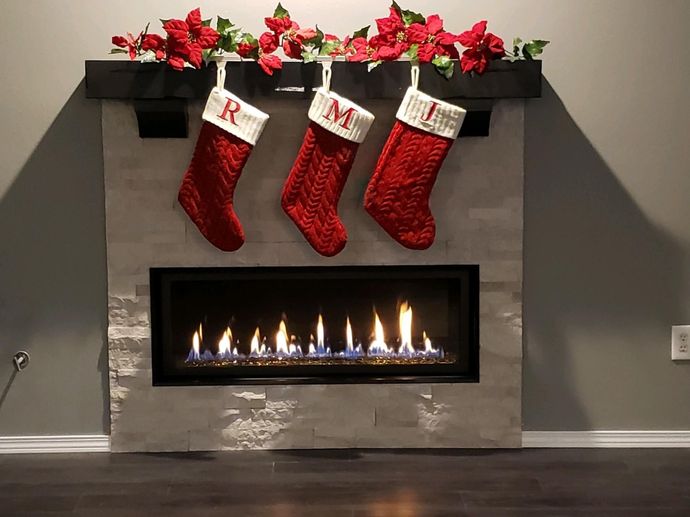 Three red stockings hang over a modern fireplace with lit flames and red holiday decorations on the mantel.