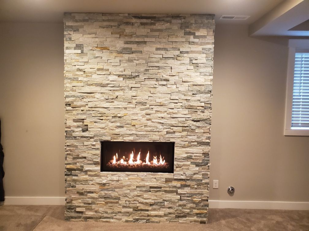 Living room with a stone fireplace and lit gas fire, gray walls, and a window with blinds.