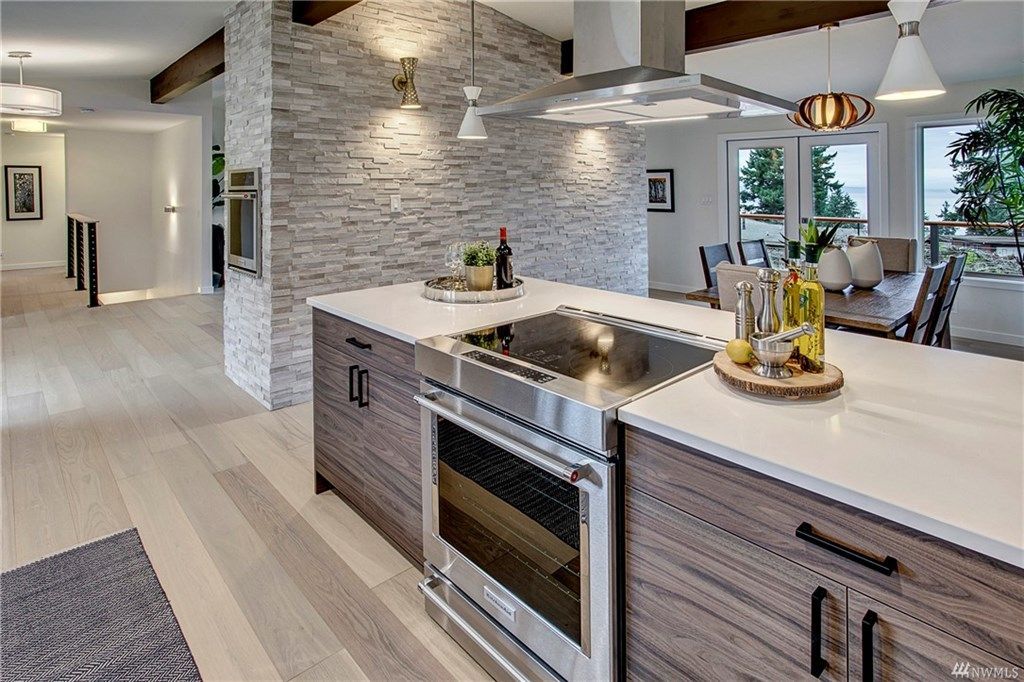 Modern kitchen with stone accent wall, white island, built-in oven, and bright open living area