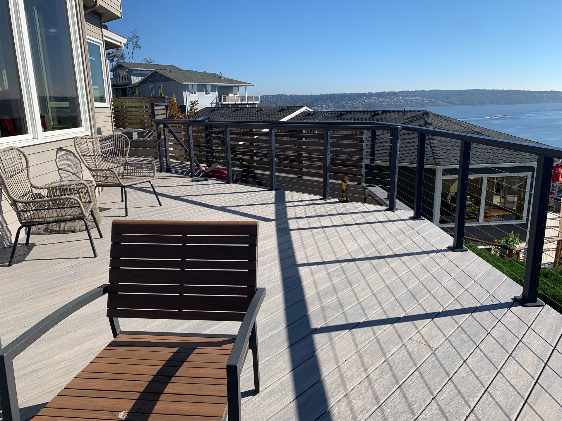 Sunny waterfront deck with metal railing, chairs, and a view of the bay and distant hills