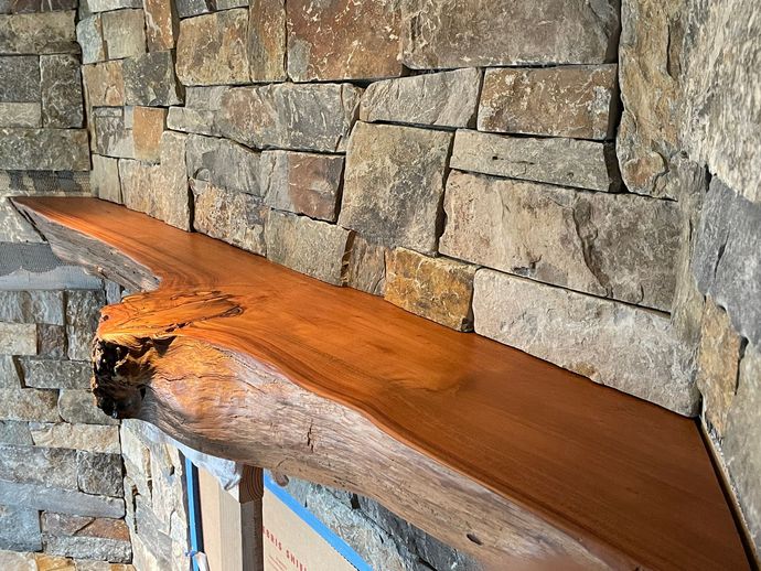 Wooden live-edge bench with glossy orange finish against a stacked-stone wall