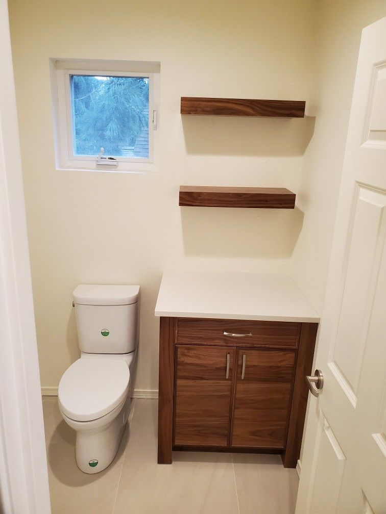 Small bathroom with toilet, wood vanity, two floating shelves, and a frosted window.