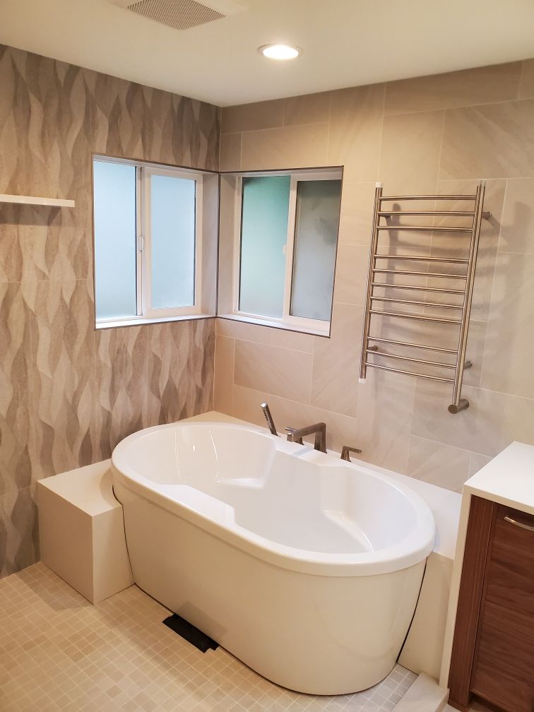 Modern bathroom with a freestanding tub, tiled walls, windows, and a towel rack