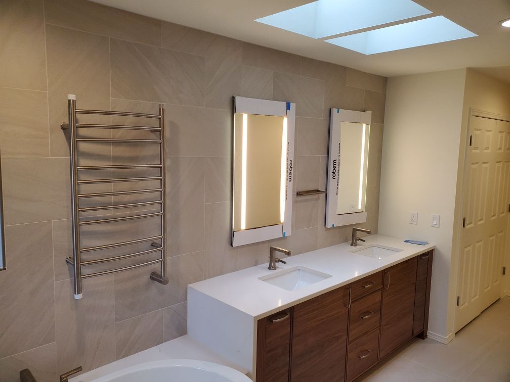 Modern bathroom with double vanity, wall mirror lights, towel rack, and beige tile walls.