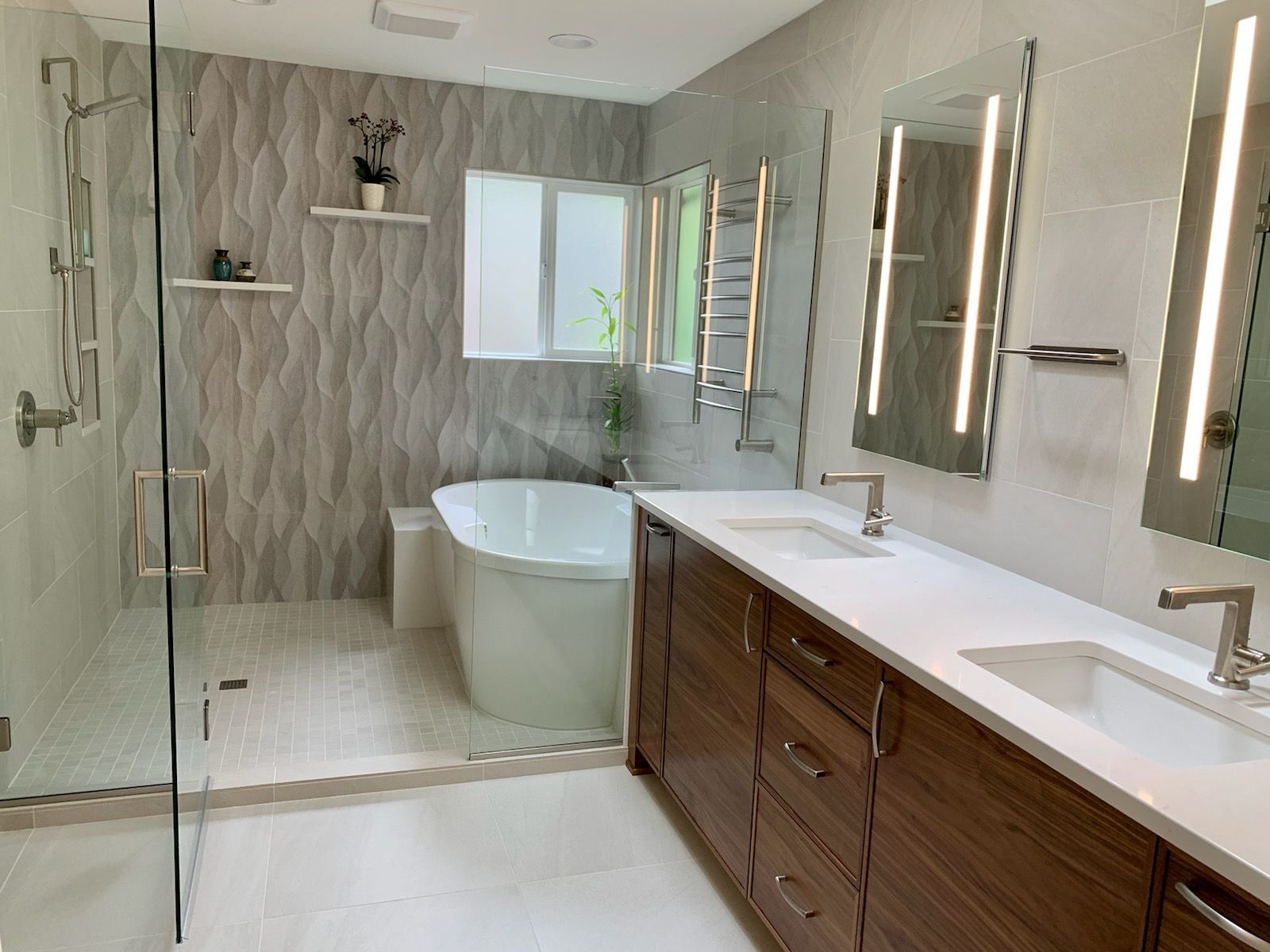 Modern bathroom with glass shower, freestanding tub, and long double vanity in gray and wood tones