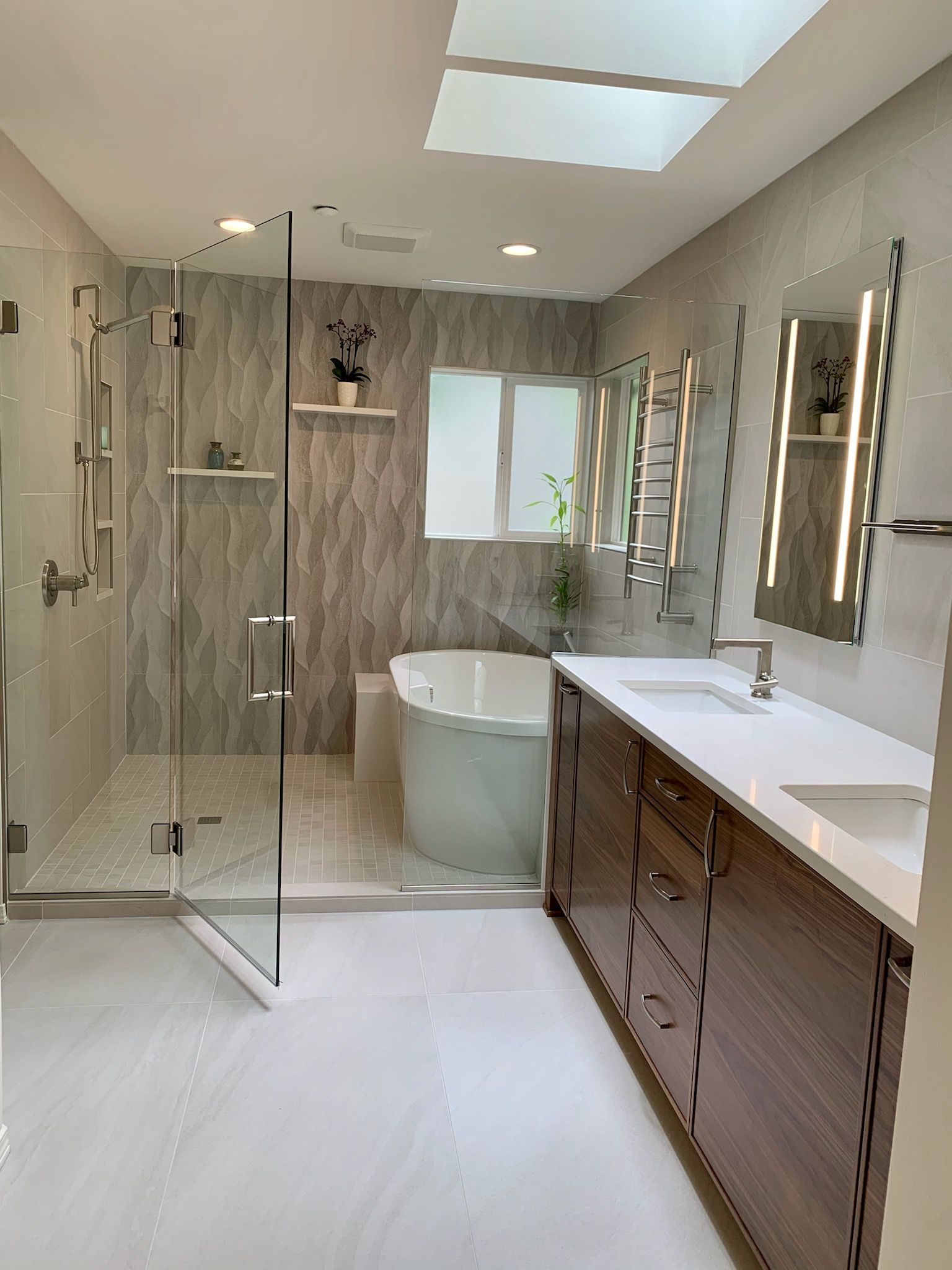 Bright modern bathroom with glass shower, freestanding tub, double vanity, and large mirror