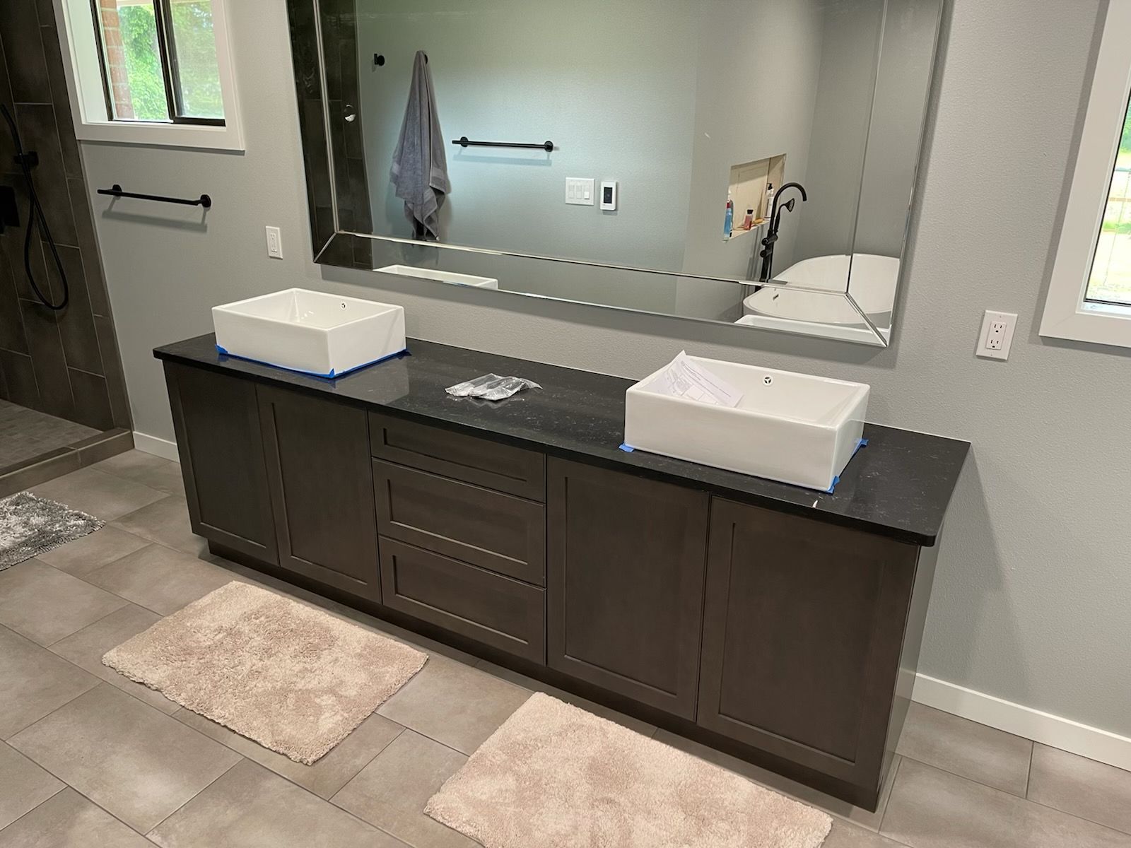 Modern bathroom vanity with dark wood cabinets, double sinks, large mirror, and beige rugs