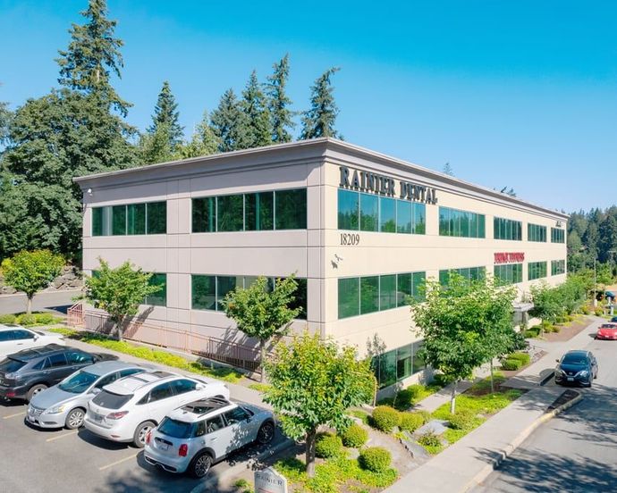 Two-story office building with parked cars, trees, and a clear blue sky