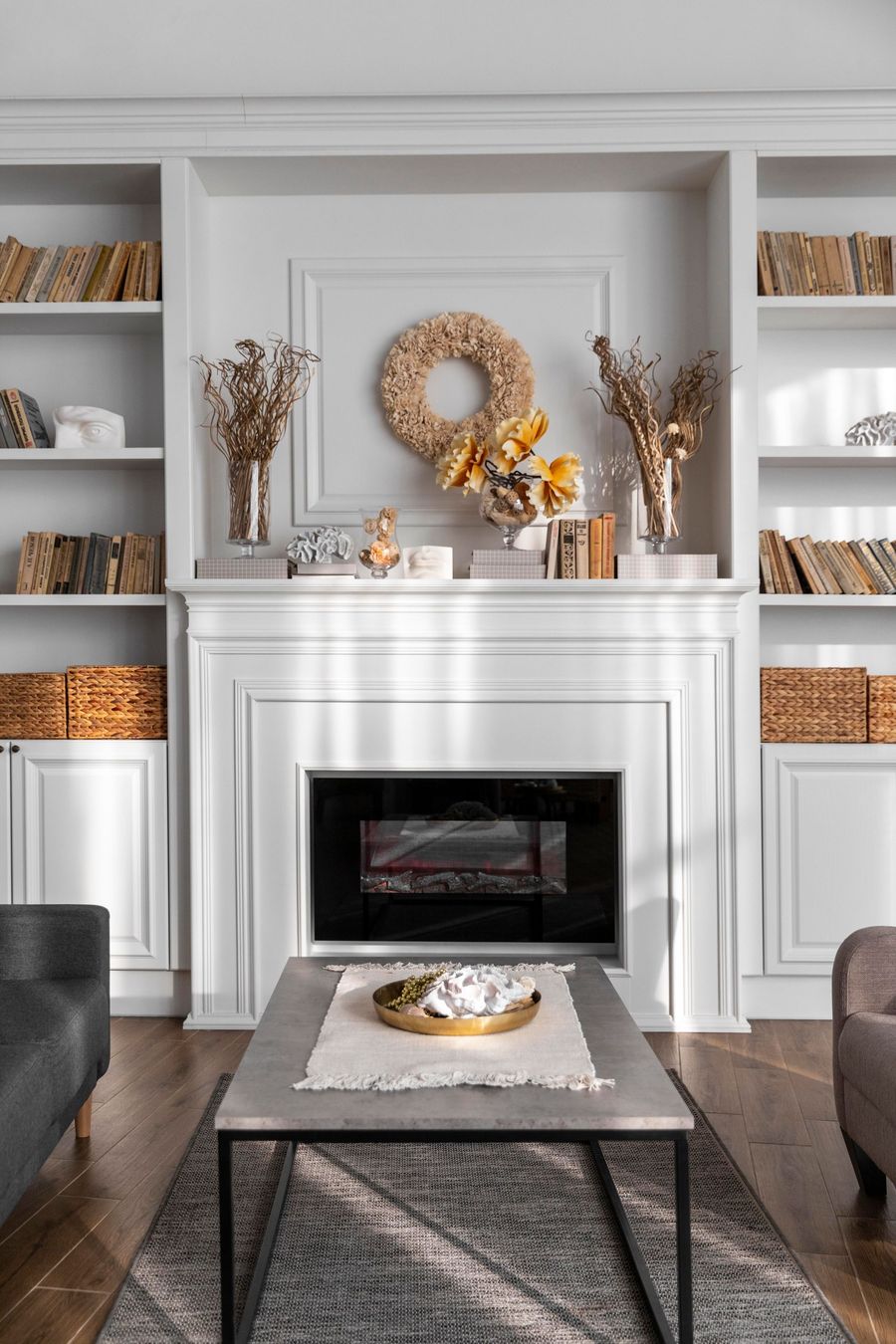 Bright white living room with a decorated fireplace, shelves, and a coffee table with fall decor