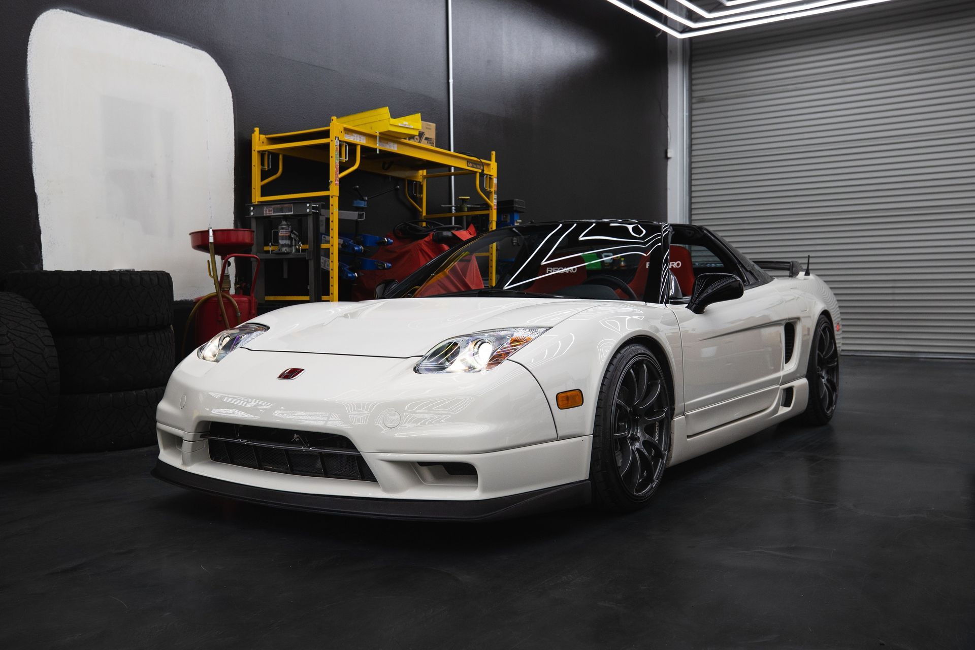White sports car in a dark garage, with a yellow lift and black wheels.