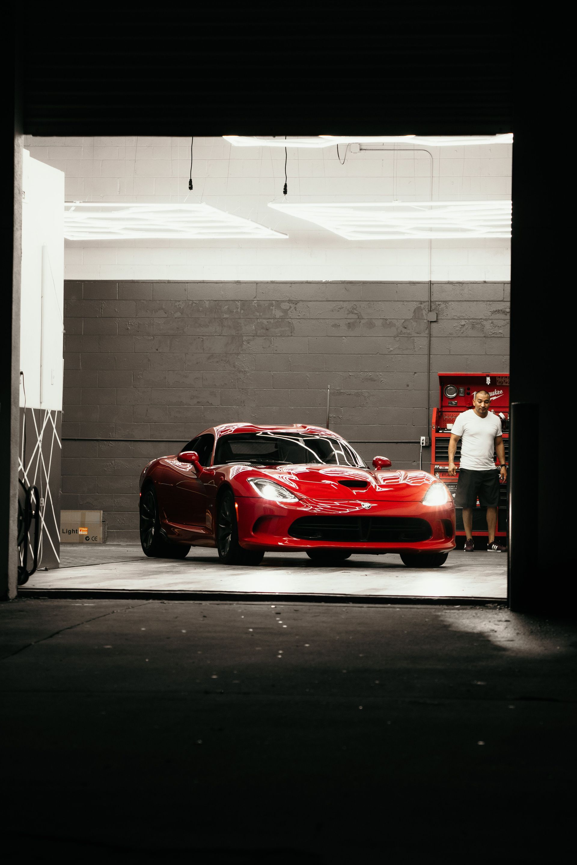 Red sports car parked in a garage, with a person standing beside it.