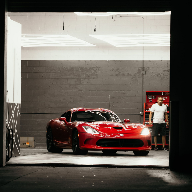 Red sports car in a garage with a man standing beside it